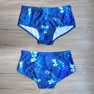 Flat lay of men's swimming trunks with tropical green leaf and white floral prints