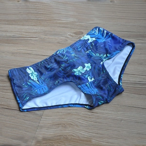 Detailed view of men's swim trunks with tropical leaf print on wooden floor background