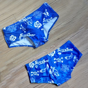 Close-up of blue men's swim trunks with white skull and sailboat prints on wood surface