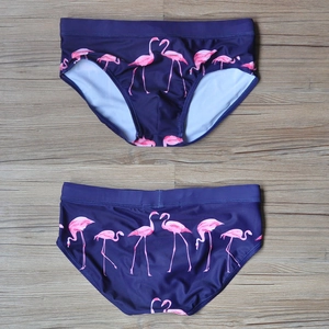 Flat lay of men's swim briefs with pink flamingo print on navy blue quick-dry fabric
