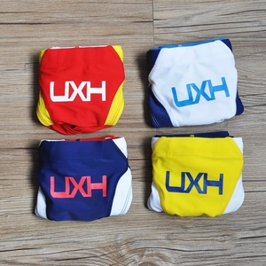 Detail view of multicolored patchwork athletic swim trunks with UXH logo on wooden floor
