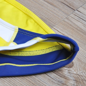 Close-up of yellow and blue patchwork men's swim briefs showing reinforced stitching detail