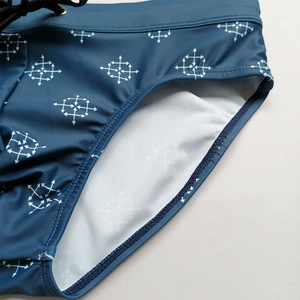 Close-up of men's navy swim briefs with white cross pattern, drawstring, and lining detail