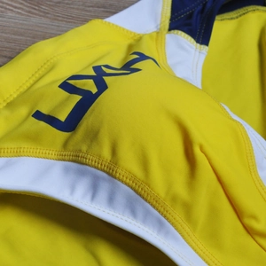 Detailed close-up of stitching and logo on color-block swimming briefs in yellow and blue