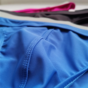 Macro detail of men's blue swim briefs showing precise double-stitch seam and elastic fabric