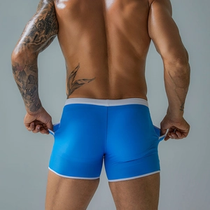 Rear view of blue men's swim trunks with white trim and side pockets on gray background