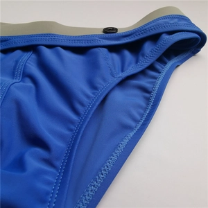 Detail of blue men's swim trunks featuring grey waistband stitching and decorative button