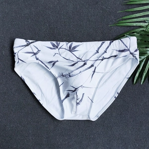 Close-up of white men's swim briefs with blue ink bamboo print on a stone background