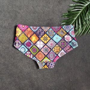 Flat lay of men's bohemian print swim trunks on dark tile with tropical palm leaf