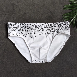 Flat lay of men's white swim briefs with black geometric pixel print on gray background