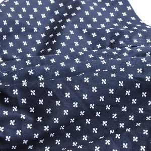 Macro shot of navy blue cotton fabric featuring white four-leaf clover floral pattern