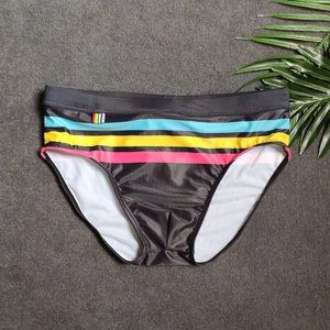 Detail view of black men's swim briefs with colorful side stripes on a grey surface