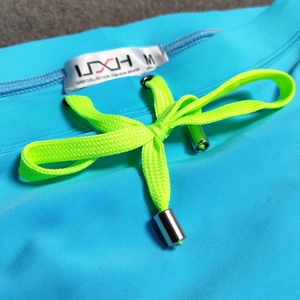 Detail of blue men's swim trunks featuring neon green drawstring and silver metal tips