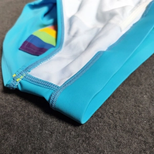 Macro detail of men's sky blue swimwear with rainbow stripe tag and breathable inner lining