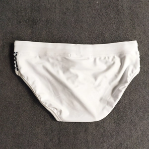 Detailed view of white men's swim briefs with black and white checkerboard side stripes