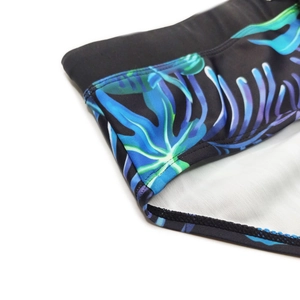Close-up of men's swim trunks featuring gradient tropical palm leaf patterns and stitching