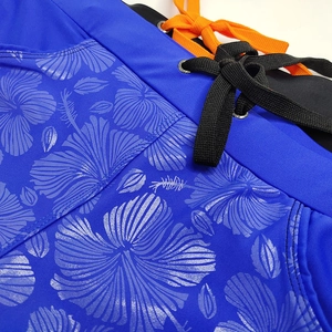 Detail of blue hibiscus print swim trunks featuring orange drawstring and metal eyelets