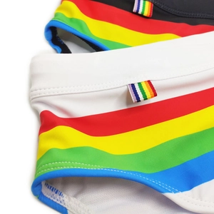 Detail of rainbow striped swimwear fabric showing woven side labels on black and white trunks