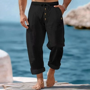 Men's loose black cotton linen drawstring pants with wood buttons shown at beach