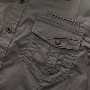 Detailed macro view of military-style shirt pocket with reinforced stitching and metal buttons