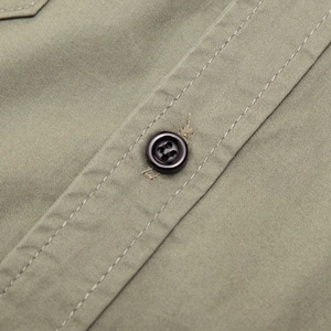 Detail view of military green cotton shirt featuring twill fabric and a black button closure