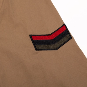 Detail of khaki cotton shirt with red, black and olive green embroidered V-shaped arm patches