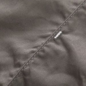 Detailed close-up of brown twill fabric with reinforced bar tack stitching on a military shirt