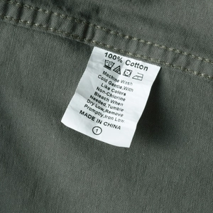 Detail of the 100% cotton wash label and twill fabric texture on an olive green shirt