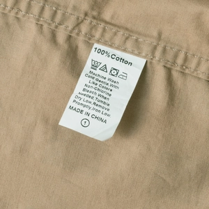 Detail of care label on 100% cotton khaki plaid shirt showing washing instructions