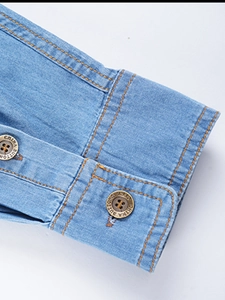 Macro detail of men's light blue denim shirt cuff with orange stitching and branded button
