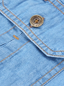 Close-up of light blue denim fabric texture and bronze metal button on pocket