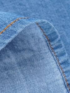 Detailed close-up of light blue denim shirt with orange contrast stitching and twill texture