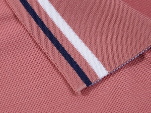 Macro detail of pink pique knit polo fabric with white and navy striped ribbed edges