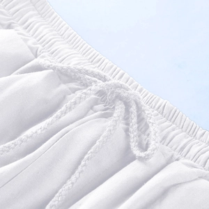 Detail of white linen beach shorts featuring elastic waistband and braided drawstring ties