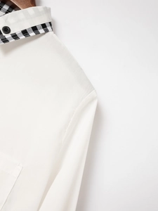 Close-up of white shirt collar with black gingham trim and sleek black button detail