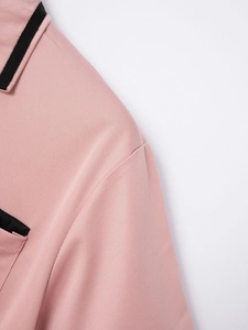 Detailaufnahme des rosa Poloshirt-Stoffs mit schwarzen Kontrastkanten an Kragen und Tasche