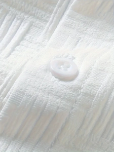 Detailed macro view of white short sleeve shirt fabric with pleated texture and button