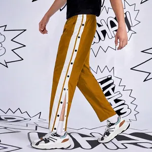 Detail of men's mustard yellow trousers with side white stripes and black snap buttons