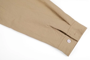 Detail of khaki linen shirt cuff featuring a semi-transparent button and neat stitching