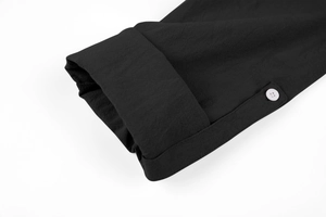 Detail of the black shirt sleeve featuring a white button and high-quality fabric texture