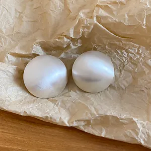 Boucles d'oreilles puces en métal argenté brossé au design géométrique minimaliste sur papier
