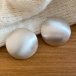 Détail rapproché de boucles d'oreilles clous bombées en métal brossé argenté.