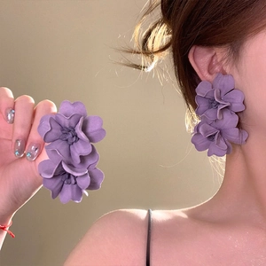 Macro view of elegant purple fabric flower drop earrings worn by a female model.