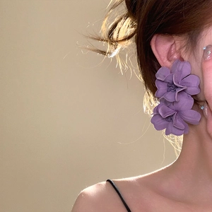Detailed close-up showing the soft texture of purple fabric flower drop earrings worn by a model.