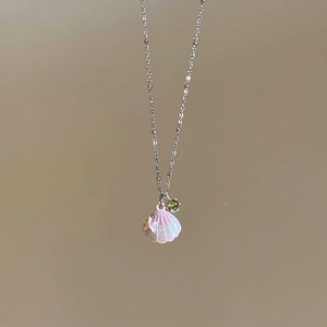 Dettaglio di una collana in acciaio con ciondolo a conchiglia rosa e zircone verde.