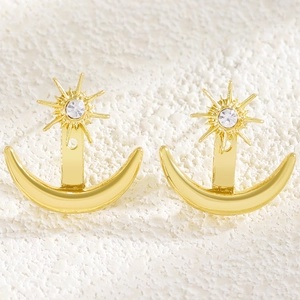 Macro detail of minimalist gold sun and moon stud earrings featuring clear crystals.