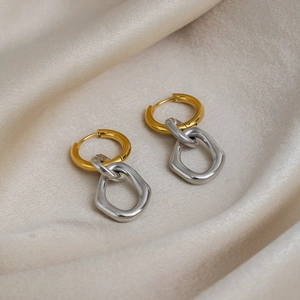 Close-up of elegant two-tone geometric hoop earrings on champagne silk background