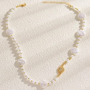 Primo piano di una collana di perle barocche con un ciondolo a fiore dorato unico.