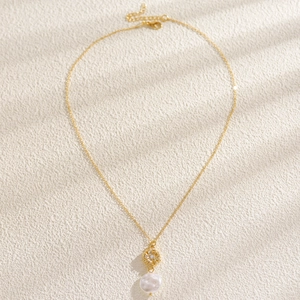 Dettaglio di collana con perle barocche e ciondolo floreale dorato su superficie