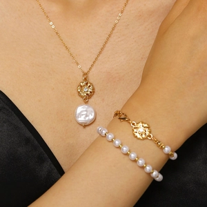 Primo piano di un set elegante con collana a fiore dorata e bracciale di perle barocche